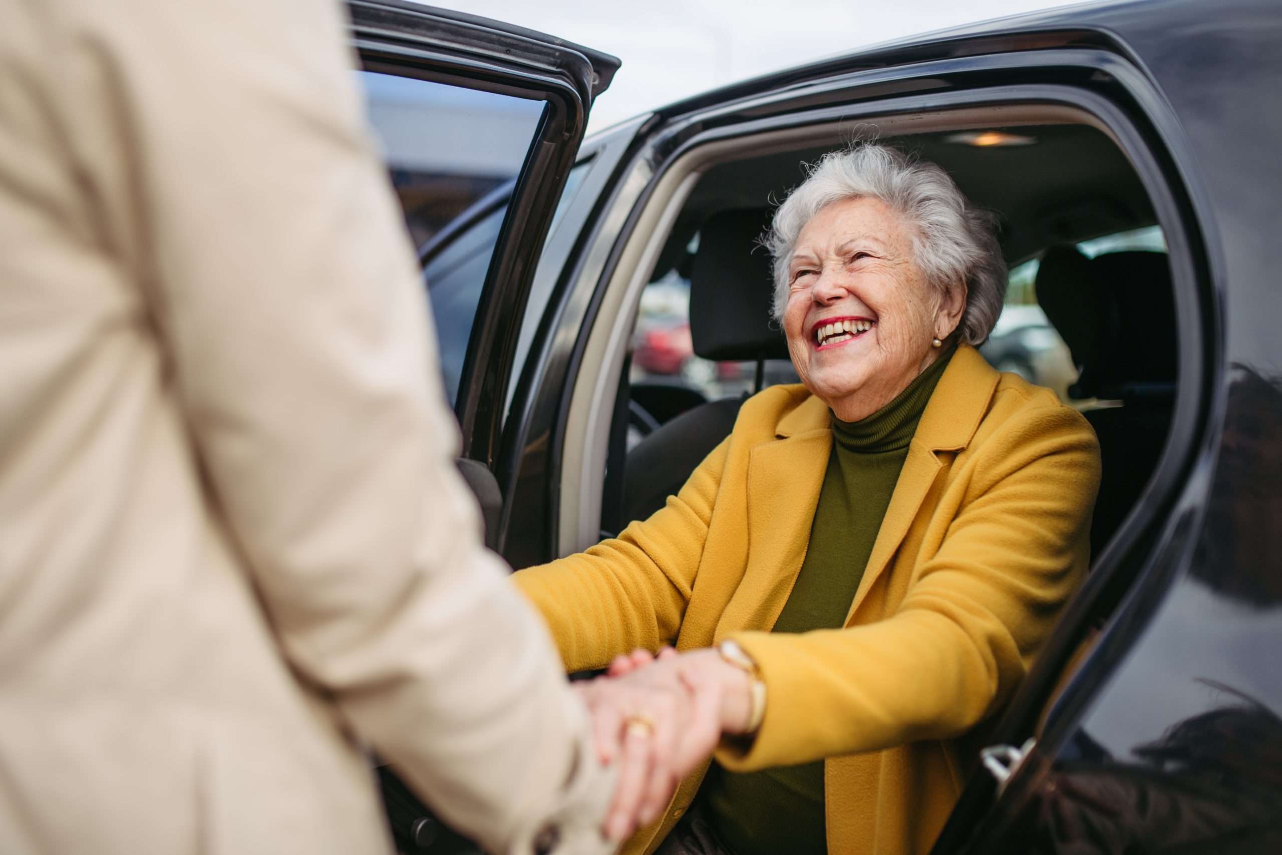 Femme aînée heureuse qui sort d'un véhicule avec de l'aide